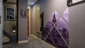 Um corredor com escada que leva ao primeiro andar, um quadro na parede à esquerda e um grande mural com vista urbana à direita.
