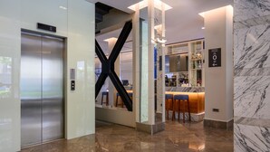 Um hall moderno com piso de mármore, elevador, balcão de recepção e área de bar.