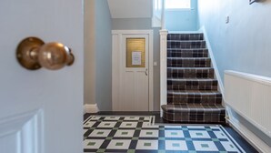 Un pasillo con piso estampado, una puerta con manijas de latón y una escalera con alfombra a cuadros.