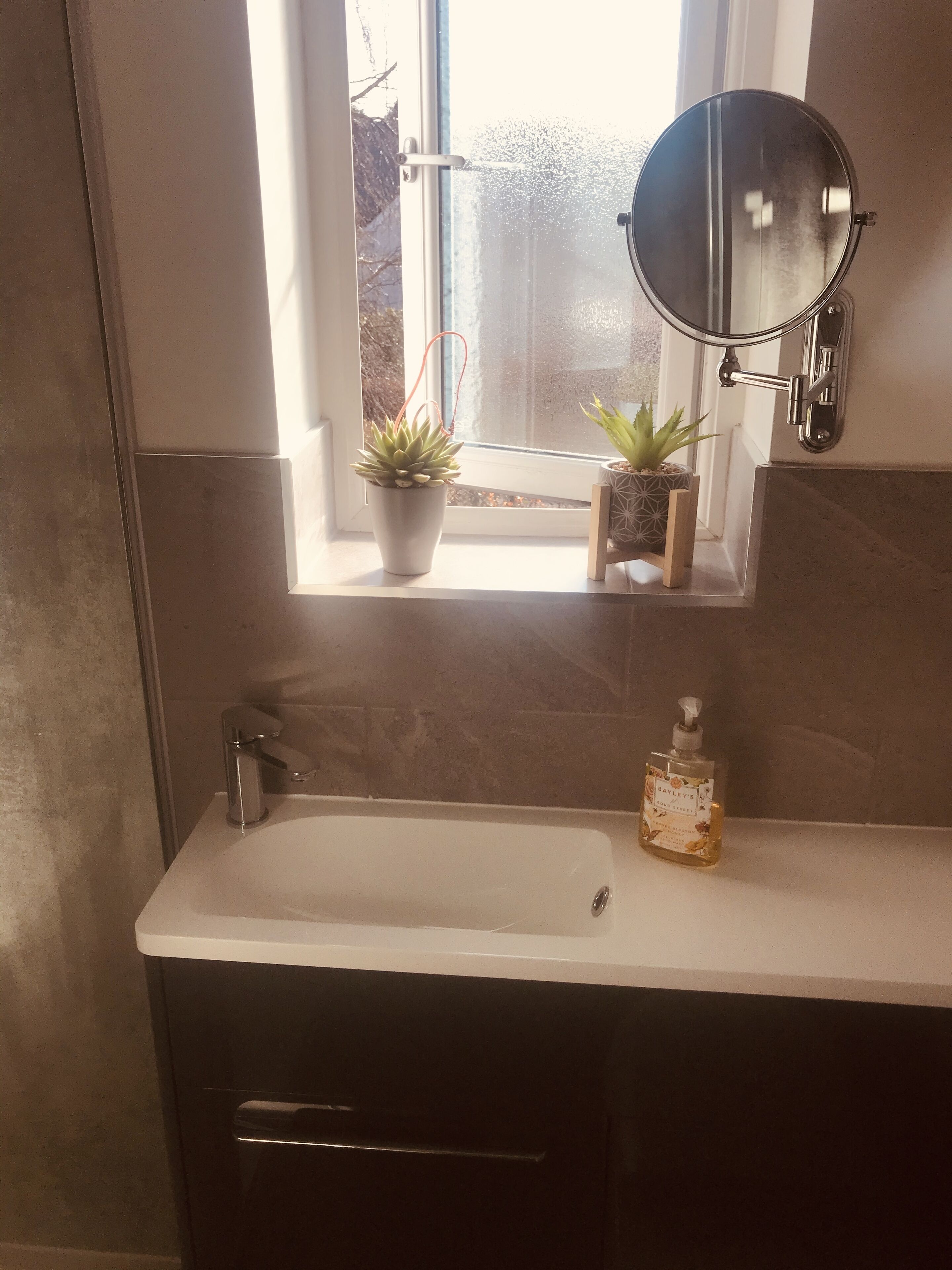 A bathroom with a white sink, a round mirror, and two potted plants on the windowsill.