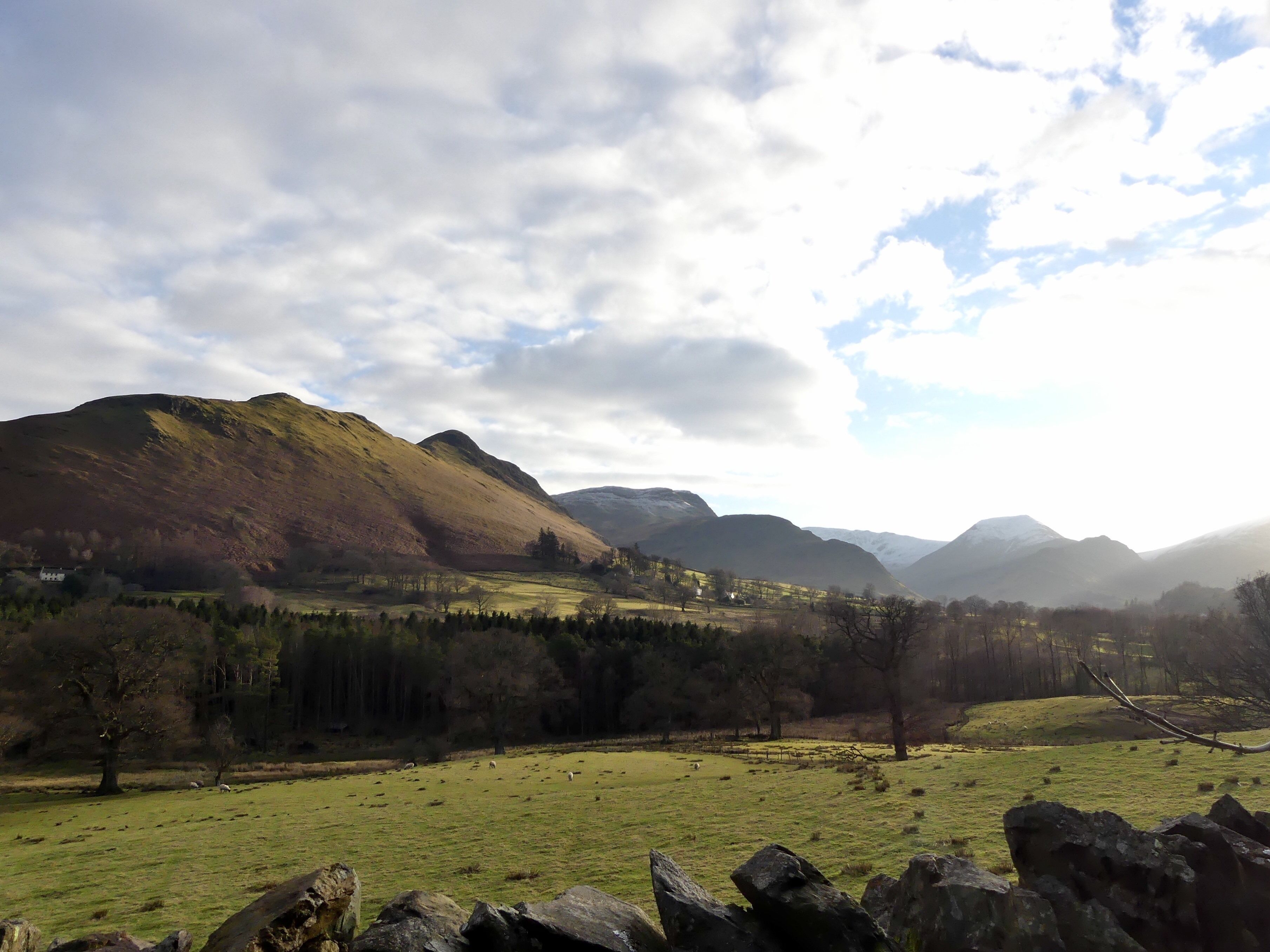 A mountainous landscape with a grassy field and a stone wall in the foreground.