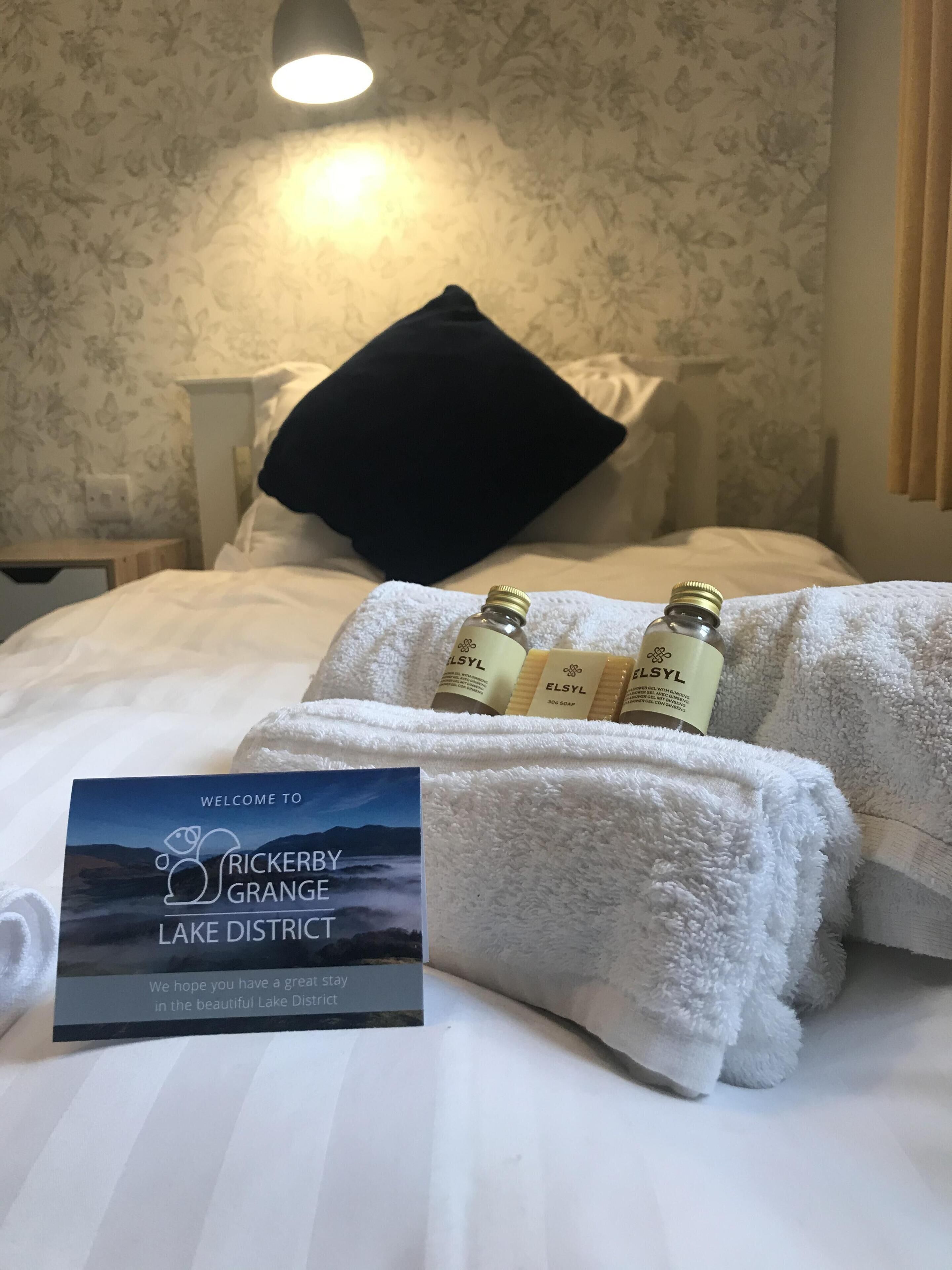 Habitación de hotel con una cama bien hecha, un cartel de bienvenida y artículos de aseo sobre una toalla.