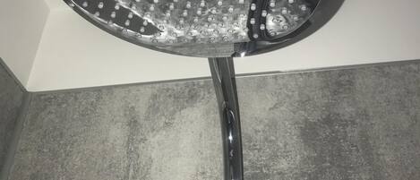 A showerhead with multiple round nozzles, mounted on a wall with a textured surface.