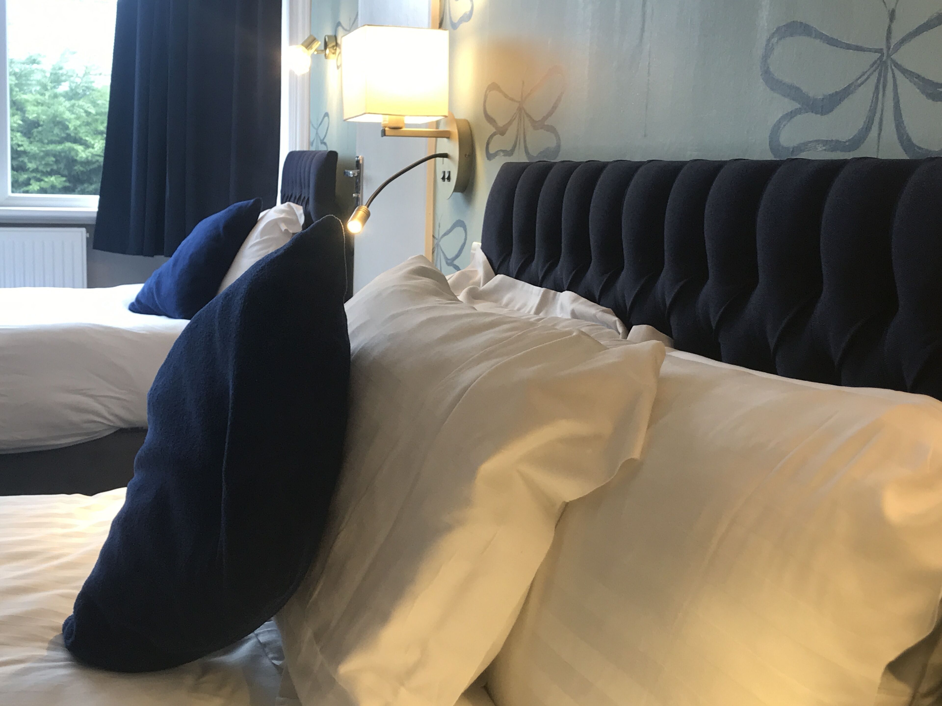 Una habitación de hotel con una cama y un cabecero oscuro, ropa de cama blanca.