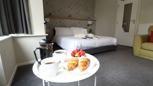 Habitación de hotel con cama, una mesita con croissants y café, un sofá y una ventana con cortinas.