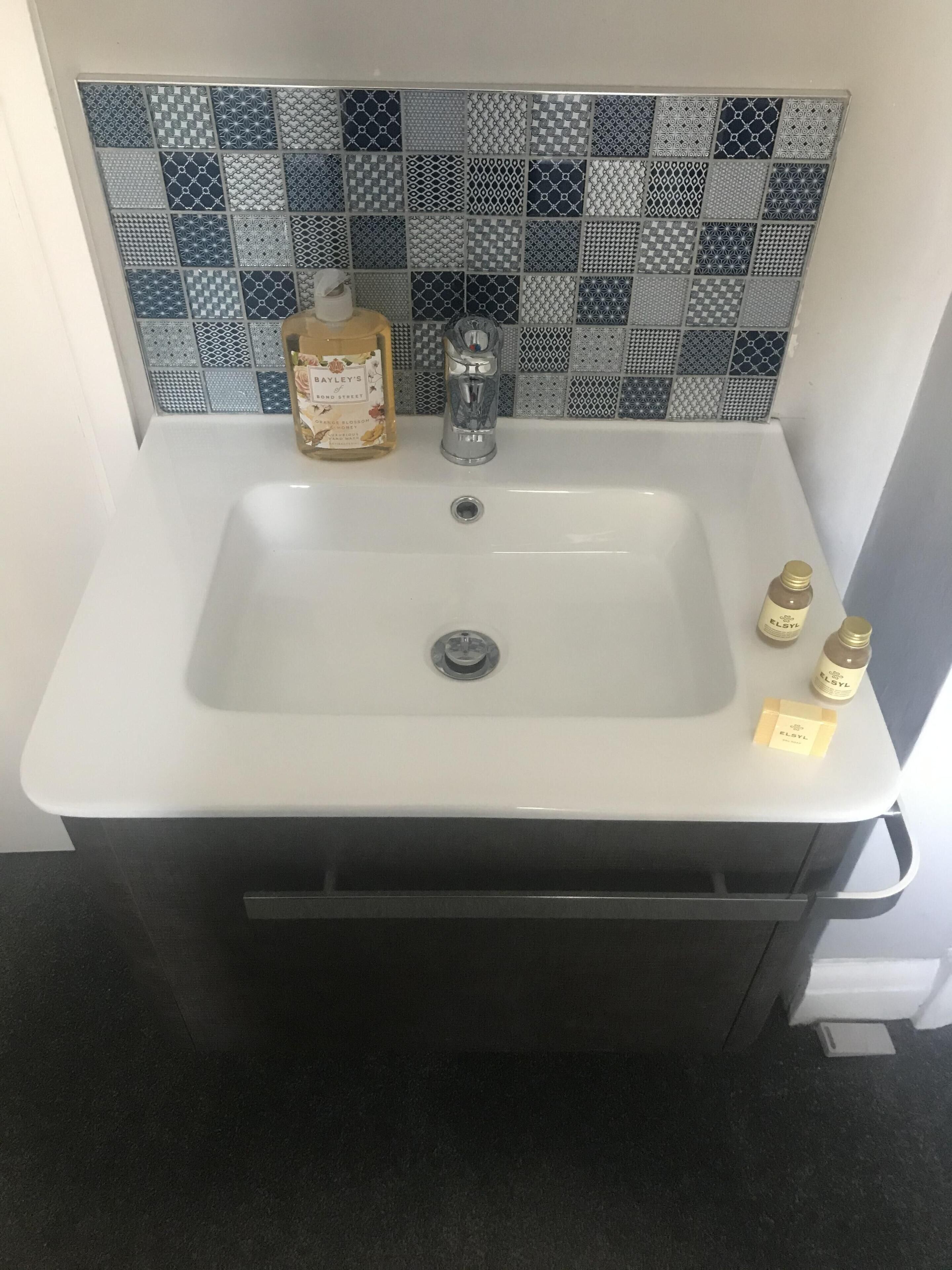 Une salle de bain avec un lavabo blanc, un pare-chocs en carreaux à motifs et des articles de toilette posés sur le comptoir.