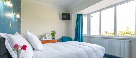 Un dormitorio con una cama, una mesita de noche, un televisor, una ventana con cortinas y una pared con un diseño azul.