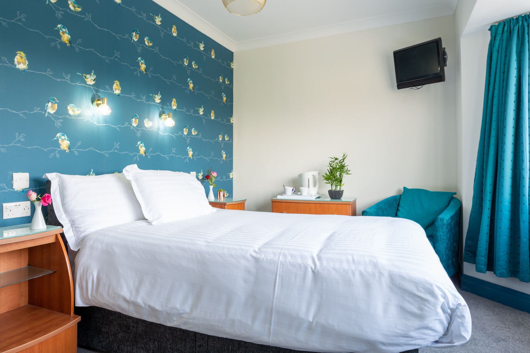 Une chambre d’hôtel avec un lit, des tables de chevet, une télévision et une fenêtre avec des rideaux.