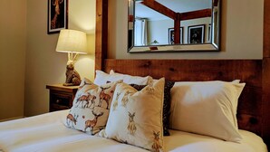 Une chambre d’hôtel avec une tête de lit en bois, un grand miroir et un lit recouvert de draps blancs et agrémenté d’oreillers décoratifs représentant des cerfs et des lapins.