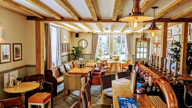Un restaurant chaleureux avec des poutres en bois, un bar doté de robinets en cuivre et des sièges confortables.