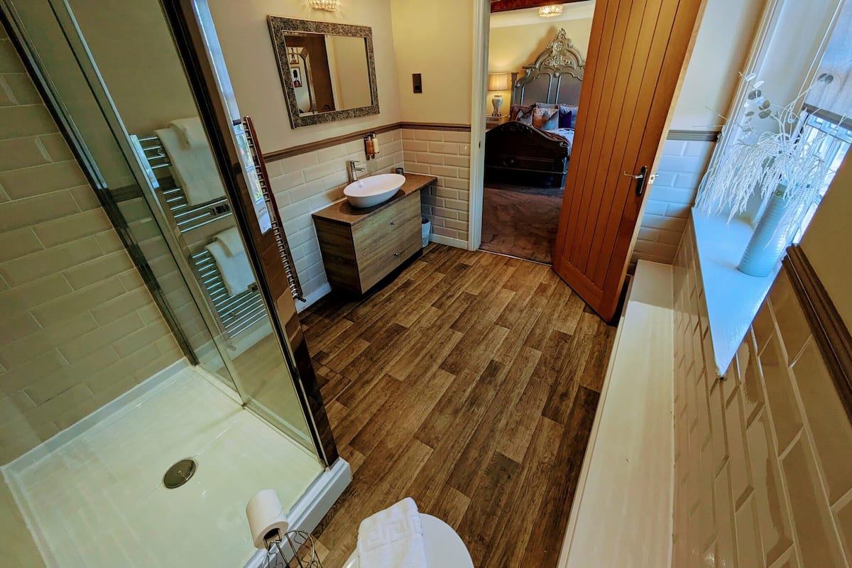 A bathroom with a wooden floor, a sink, a mirror, and a shower area.