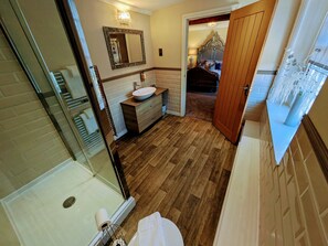 A bathroom with a wooden floor, a sink, a mirror, and a shower area.