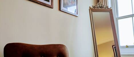 Una habitación con un sillón marrón, dos cuadros en la pared y un espejo grande que refleja una lámpara y una estatua.
