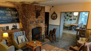 L’intérieur chaleureux d’un pub typique, avec une cheminée en briques, une tête de cerf accrochée au mur et un panneau indiquant qu’une salle est disponible à la location pour des événements.