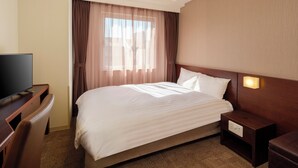 Ein Hotelzimmer mit Bett, Fernseher, Nachttisch und einem Fenster mit Vorhängen.