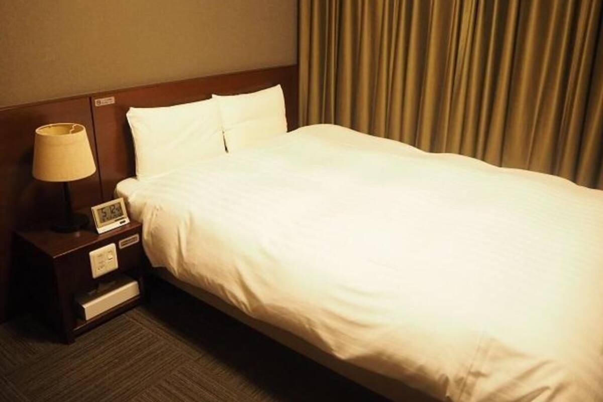 A hotel room with a bed, a nightstand with a lamp, and a digital clock.