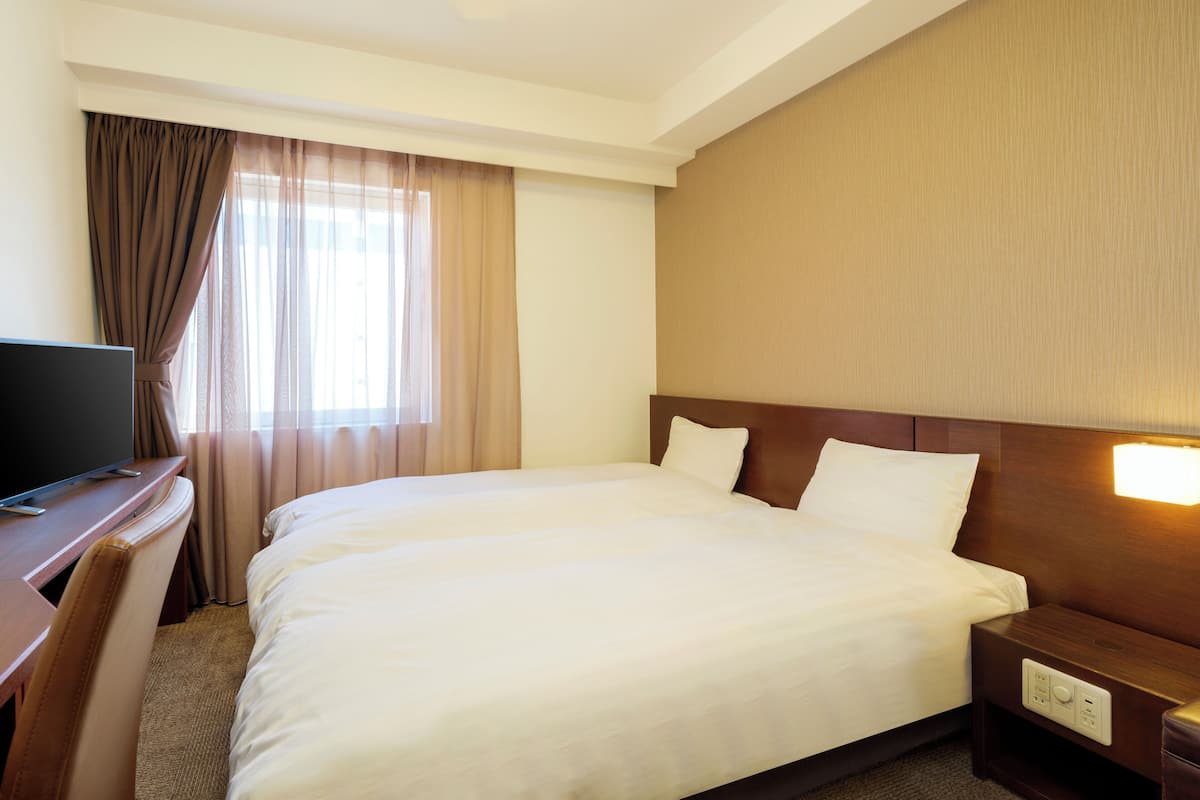 A hotel room with a large bed, a desk with a television, and a nightstand with a lamp.