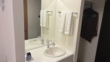 Un baño con lavamanos blanco, un espejo y dos toallas colgadas en un toallero.