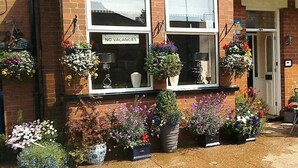 A brick building with a 'NO VACANCIES' sign, multiple flower pots, and a 'South Lodge' sign above the entrance. - South Lodge (Bridlington)