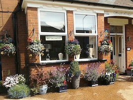 A brick building with a 'NO VACANCIES' sign, multiple flower pots, and a 'South Lodge' sign above the entrance.