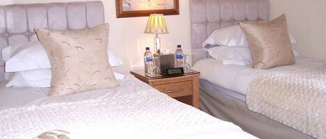 Two beds with headboards, a bedside table with a lamp, and a clock.