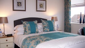 A neatly made bed with a floral-patterned bedspread, two bedside lamps, and a water bottle on the nightstand. - South Lodge (Bridlington)