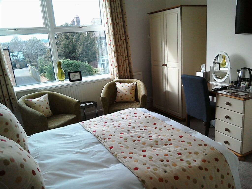 A bedroom with a bed, two armchairs, a wardrobe, a desk, and a window with curtains.