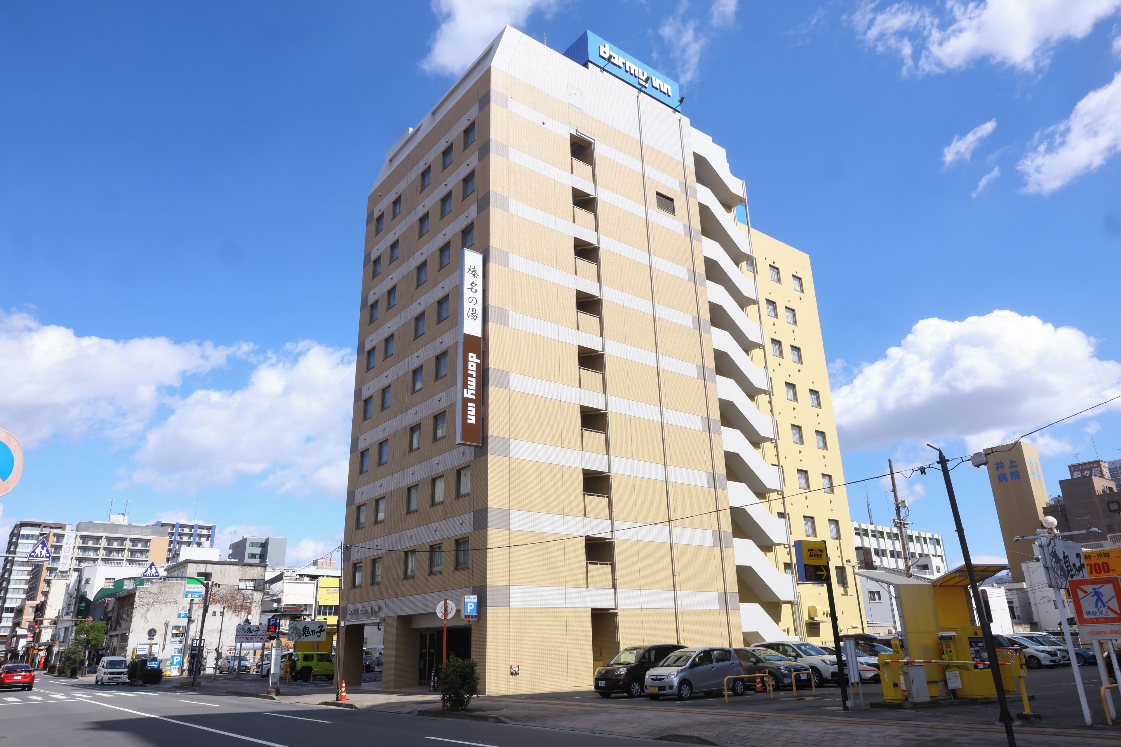 A multi-story hotel with a prominent 'Hotel Inn' sign, a parking area, and a clear blue sky.