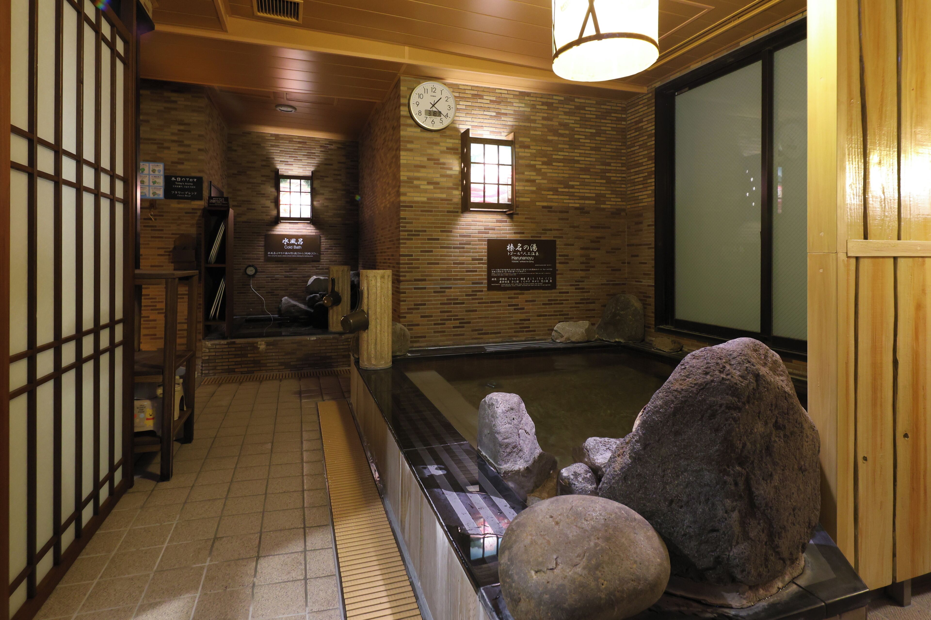Un onsen japonés tradicional con interior de madera, un baño de aguas termales de piedra y un reloj en la pared.