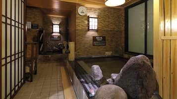 Un onsen japonés tradicional con interior de madera, un baño de aguas termales de piedra y un reloj en la pared.