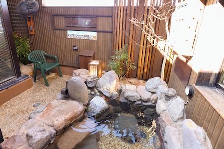 A small pond with rocks, a wooden fence, a chair, and a fan.