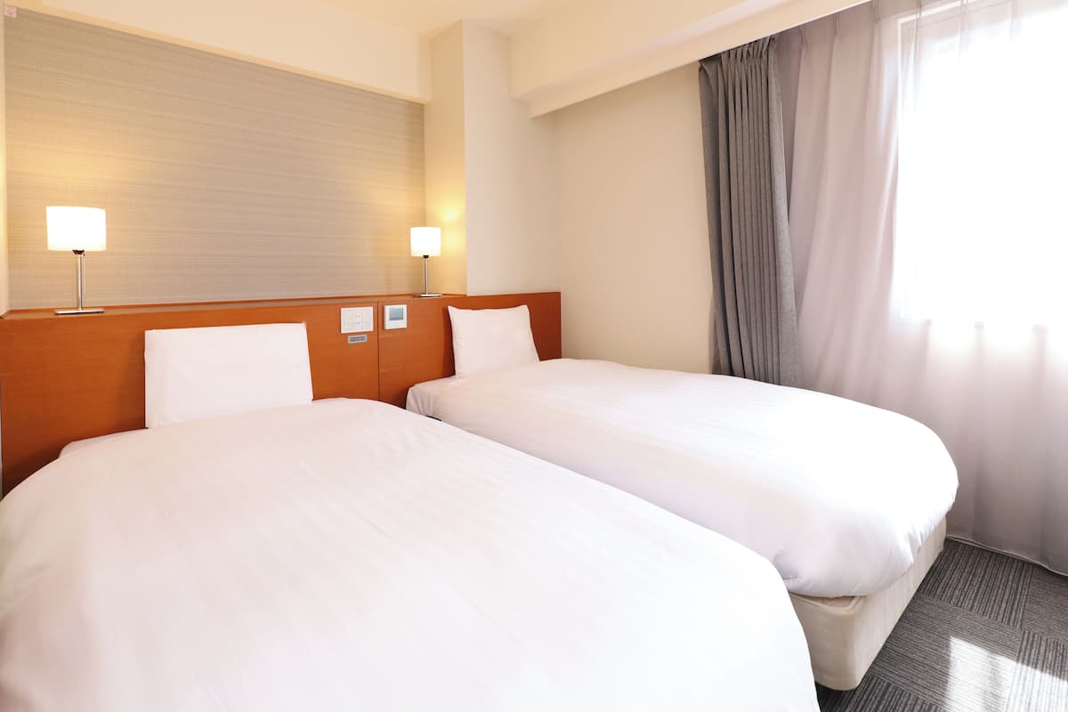 A hotel room with two beds, a wooden headboard, two bedside lamps, and a window with curtains.