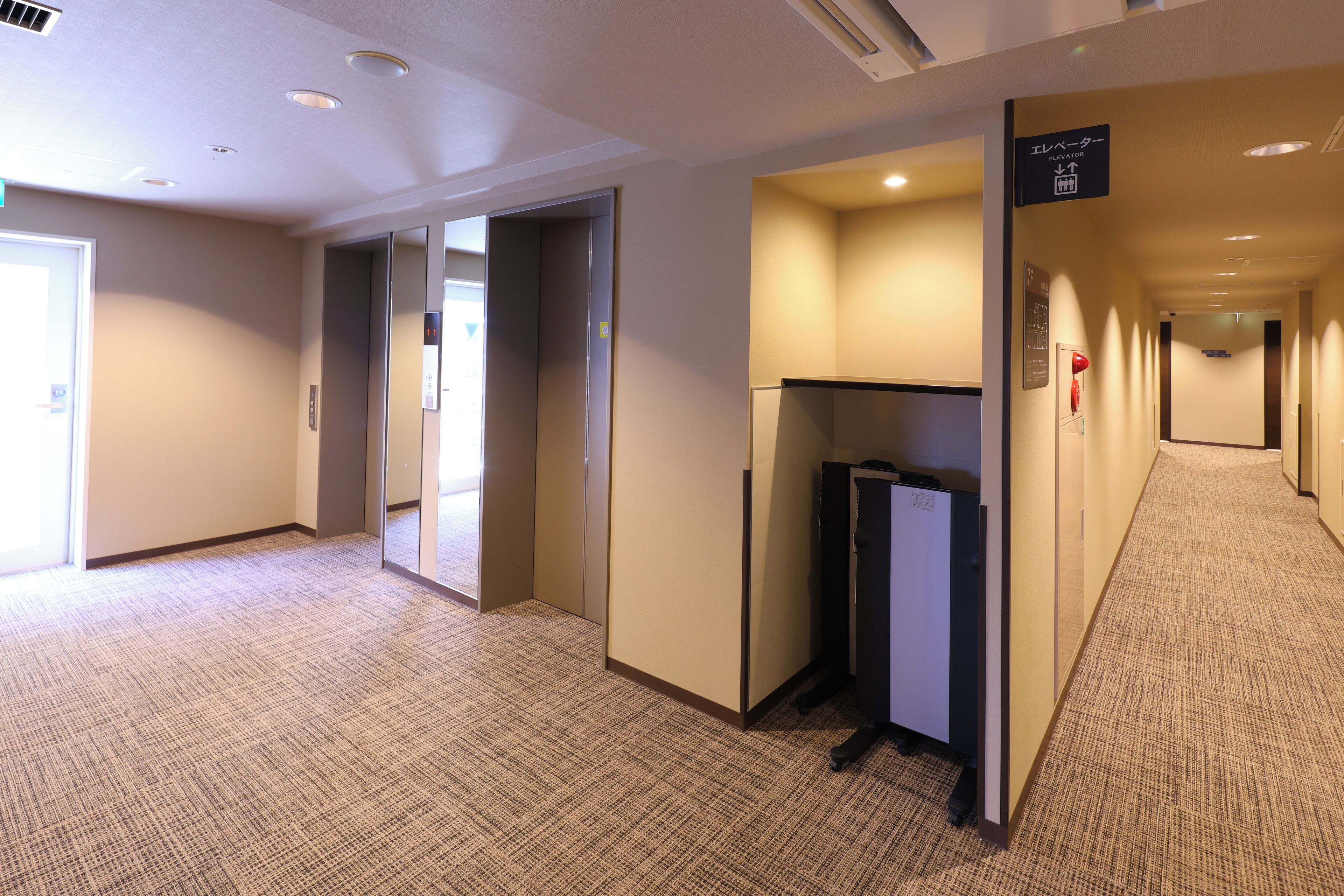 Een hotelgang met tapijtvloeren, een receptiebalie en een lift.