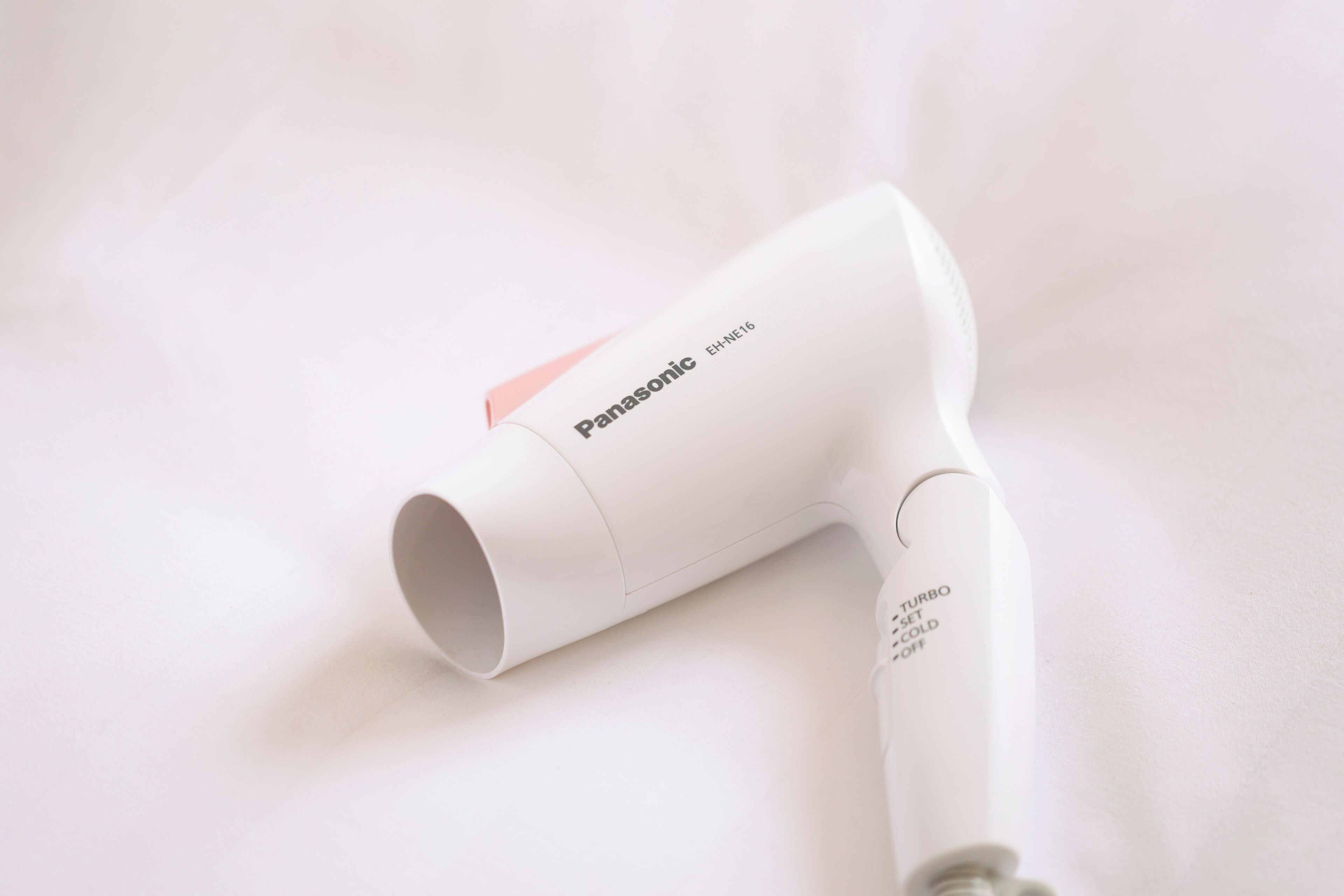 Un secador de pelo Panasonic con diseño blanco y rosa, sobre una superficie blanca.