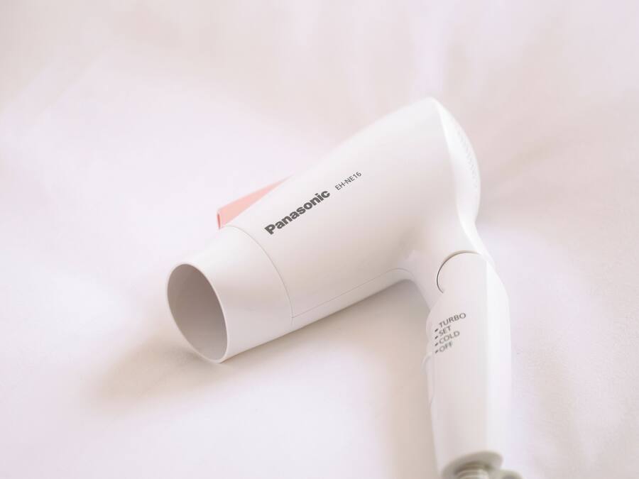 Un secador de pelo Panasonic con diseño blanco y rosa, sobre una superficie blanca.