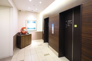 A hotel lobby with a wooden wall, a reception desk, and two elevators.