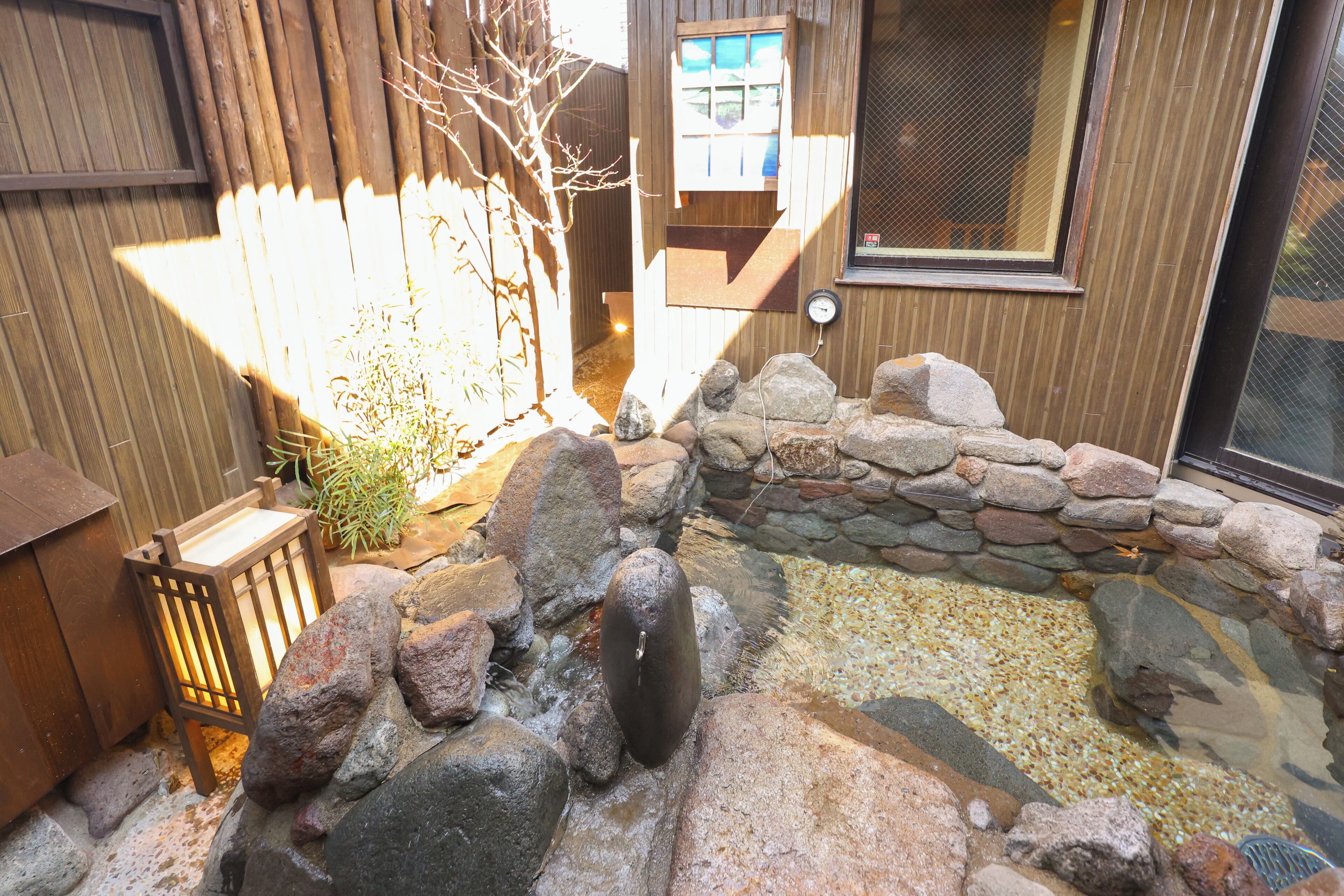A stone water feature with a wooden fence and a wooden structure with a window.