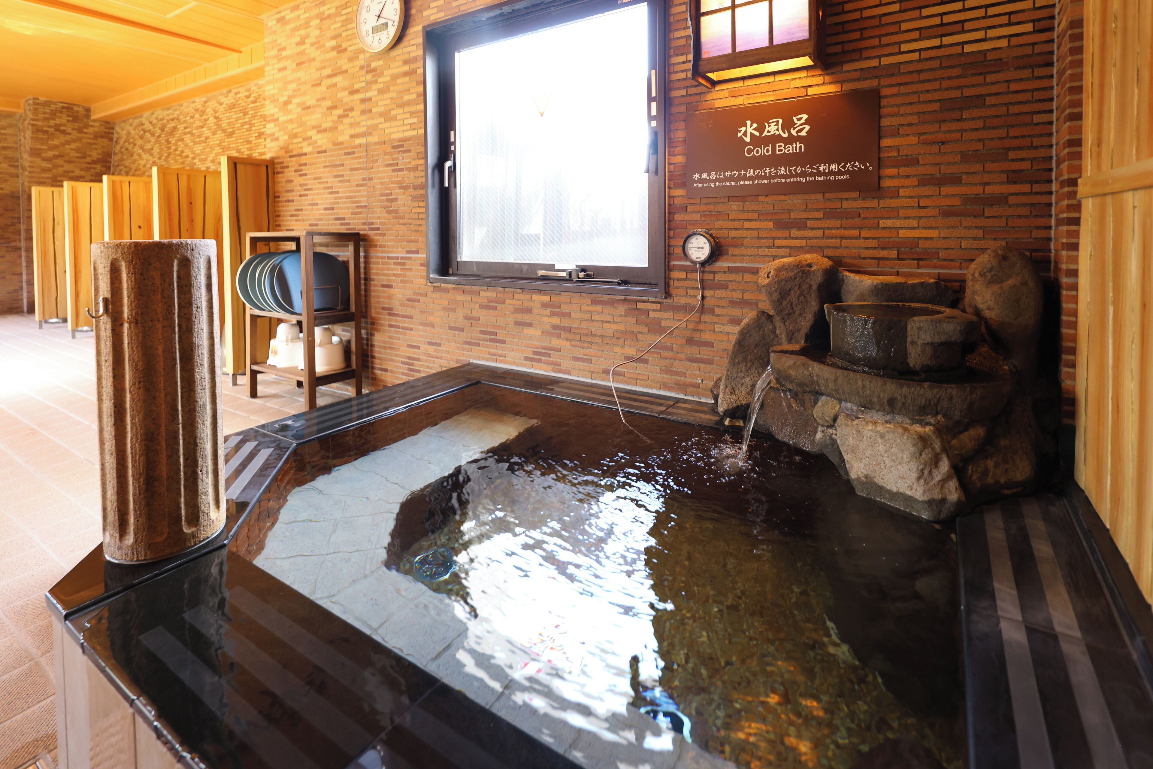 A traditional Japanese onsen with a wooden bath, a stone hot spring, and a sign indicating it is a color bath.