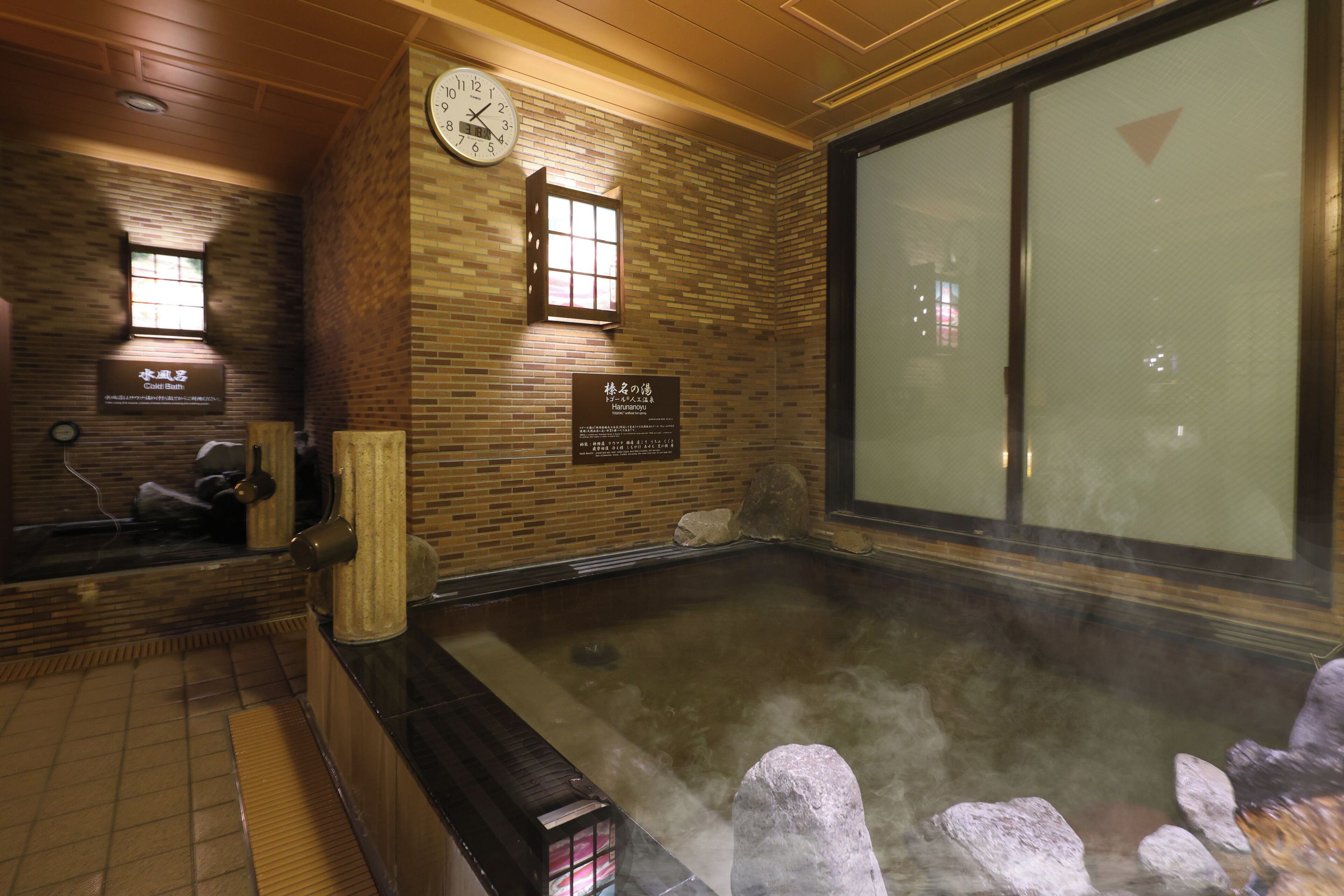 A traditional Japanese onsen with a wooden interior, a hot spring bath, and a stone seating area.
