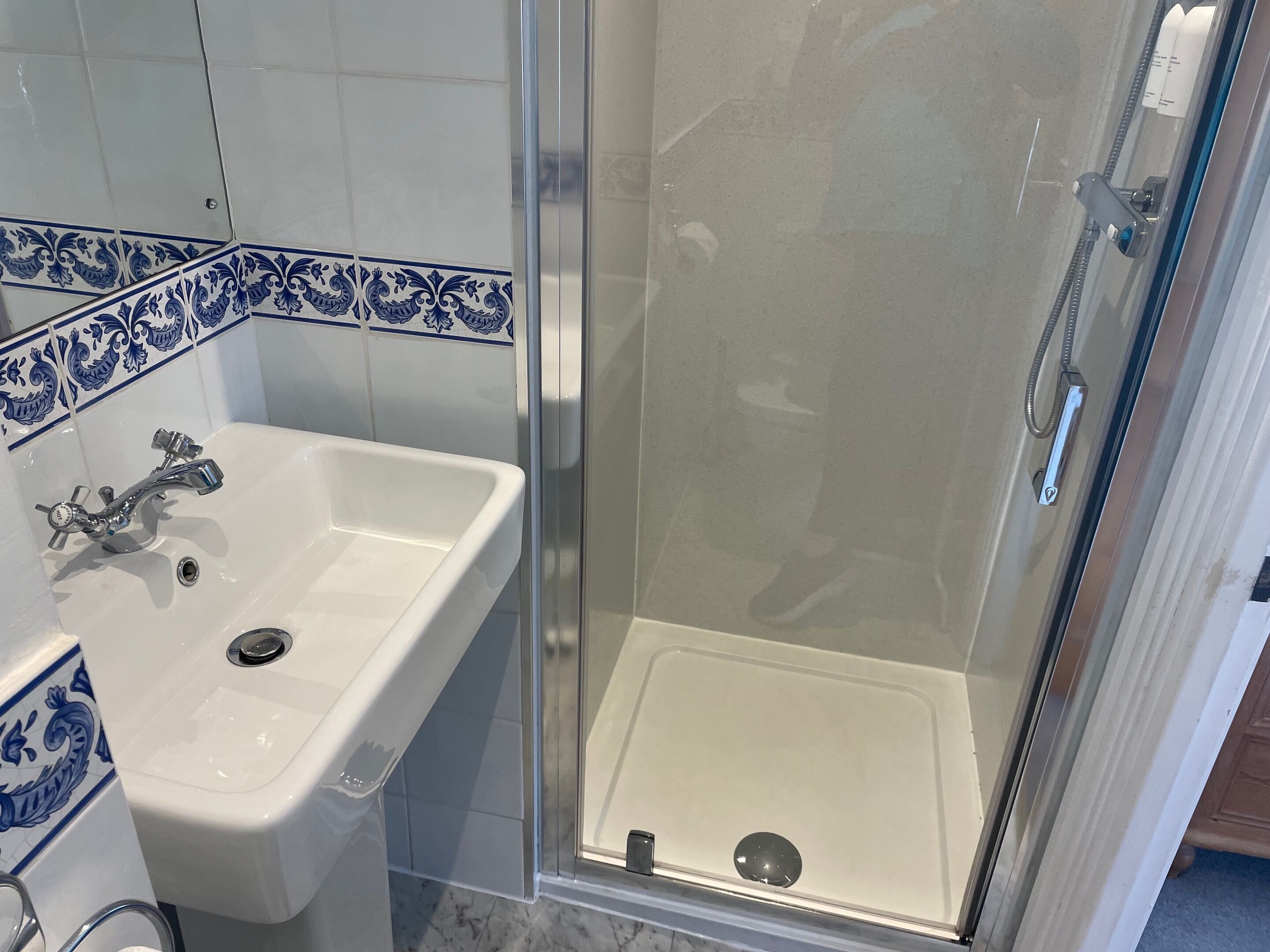 Un baño con un lavamanos blanco, una ducha con puerta de cristal y azulejos decorativos azules.