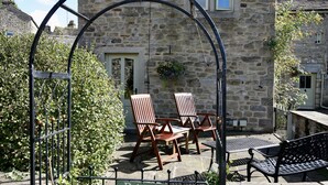 A stone building with a private entrance, two wooden chairs, a metal table, and a potted plant. - Ashfield House (Skipton)