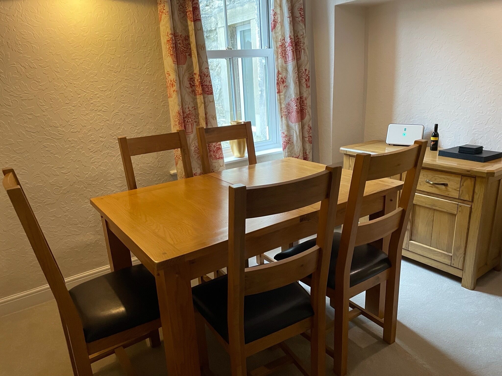 A wooden dining table with four chairs, a small wooden cabinet, and a laptop on a desk.