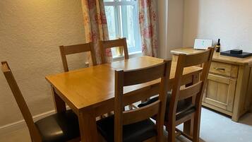 A wooden dining table with four chairs, a small wooden cabinet, and a laptop on a desk.