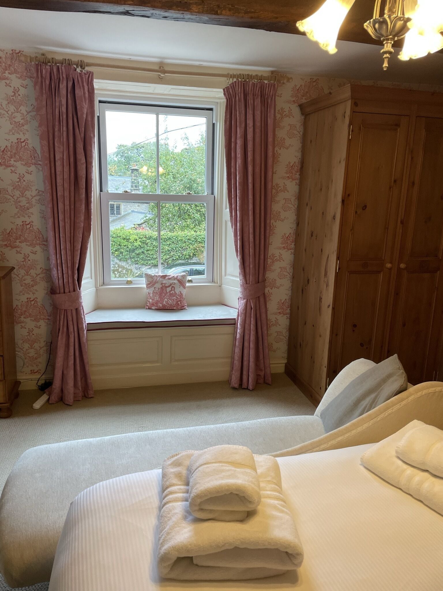 Un dormitorio con ventana, una cama con almohadas, una mesita de noche y un armario de madera.