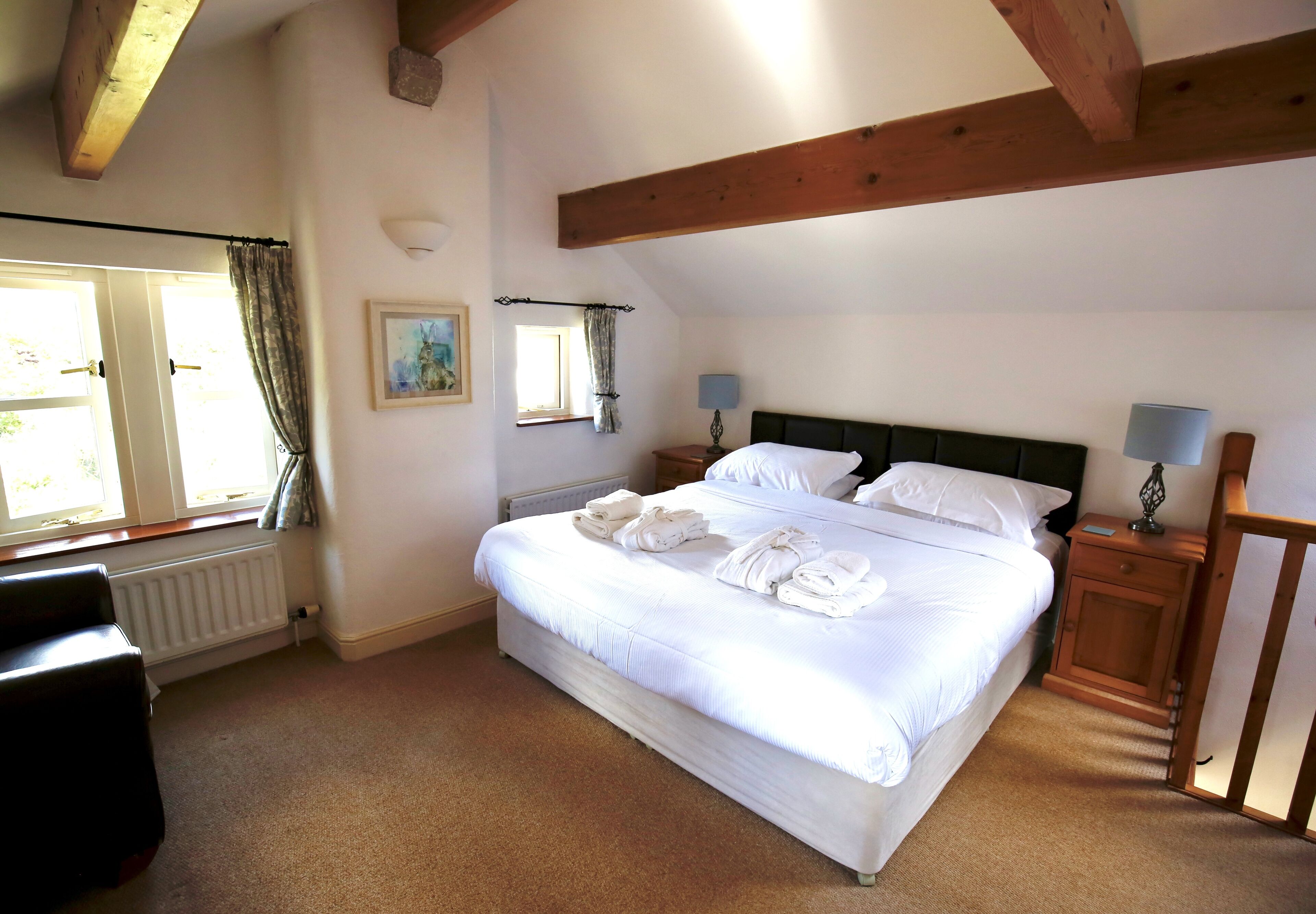 A bedroom with a large bed, two bedside tables with lamps, a radiator, and a window with curtains.