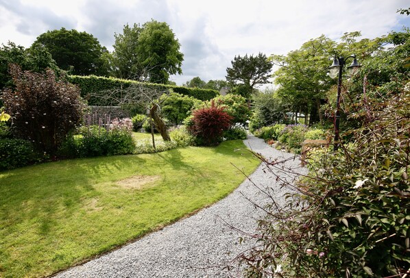 A garden pathway with a gravel surface, surrounded by various shrubs and trees.