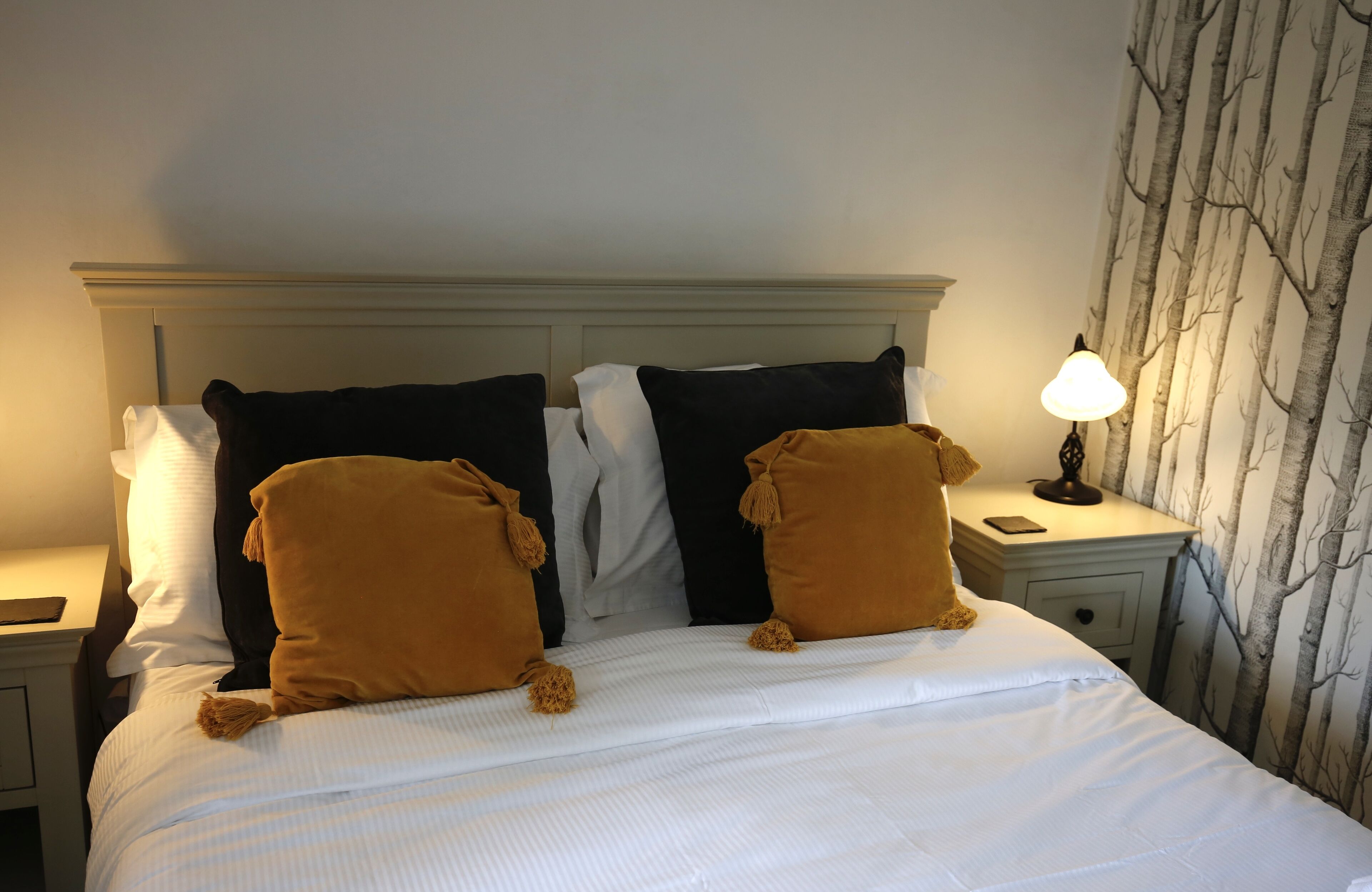 A neatly made bed with white and brown pillows, a bedside lamp, and a nightstand with a phone.