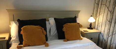 A neatly made bed with white and brown pillows, a bedside lamp, and a nightstand with a phone.