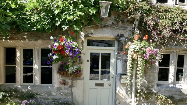 A stone building with a white door, windows, and hanging flower baskets. - Ashfield House (Skipton)