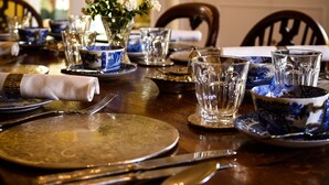 Mesa de jantar posta com pratos estampados em azul e branco, copos de vidro transparente e um vaso com flores.